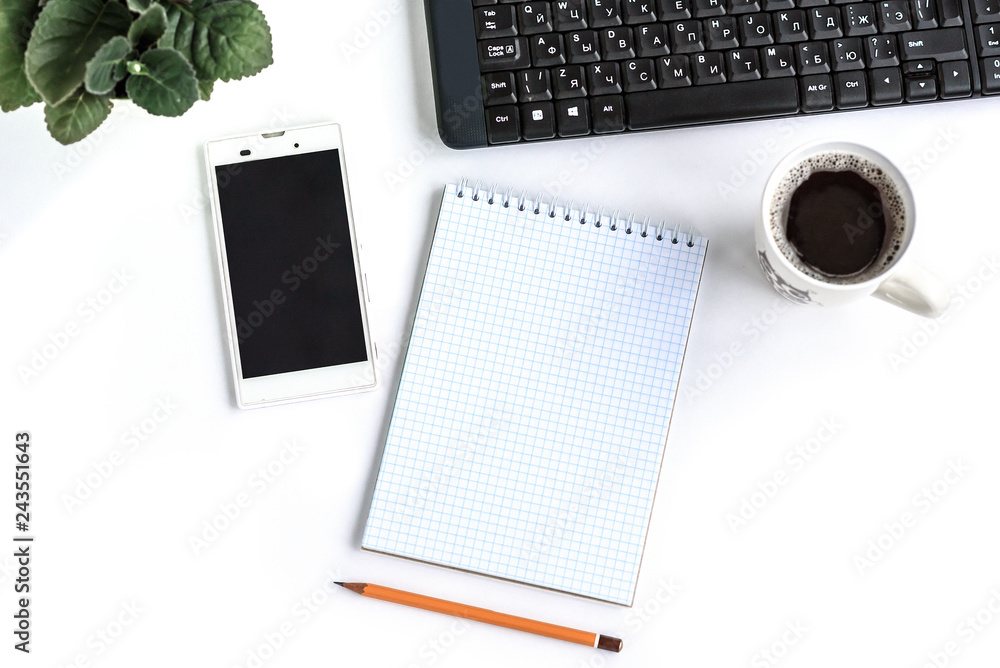 A notepad with smart phone, pencil, coffee and flowers on white table with copy space. Flatlay. A notepad with smart phone, pencil, coffee and flowers on white table with copy space. Flatlay.