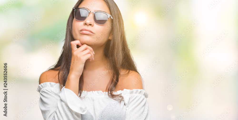 Young beautiful arab woman wearing sunglasses over isolated background with hand on chin thinking about question, pensive expression. Smiling with thoughtful face. Doubt concept. Young beautiful arab woman wearing sunglasses over isolated background with hand on chin thinking about question, pensive expression. Smiling with thoughtful face. Doubt concept.