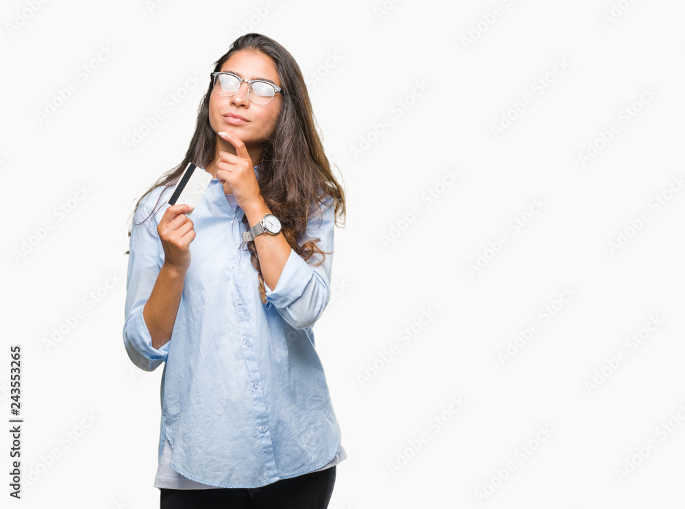 Young arab woman holding credit card over isolated background serious face thinking about question, very confused idea Young arab woman holding credit card over isolated background serious face thinking about question, very confused idea