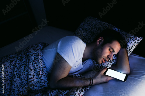 Young man using smartphone in bed at night