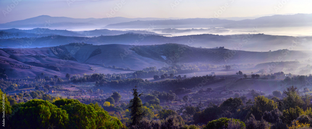 Meadow of Tuscany at misty morning. Rural landscape in fog during sunrise time and hills,