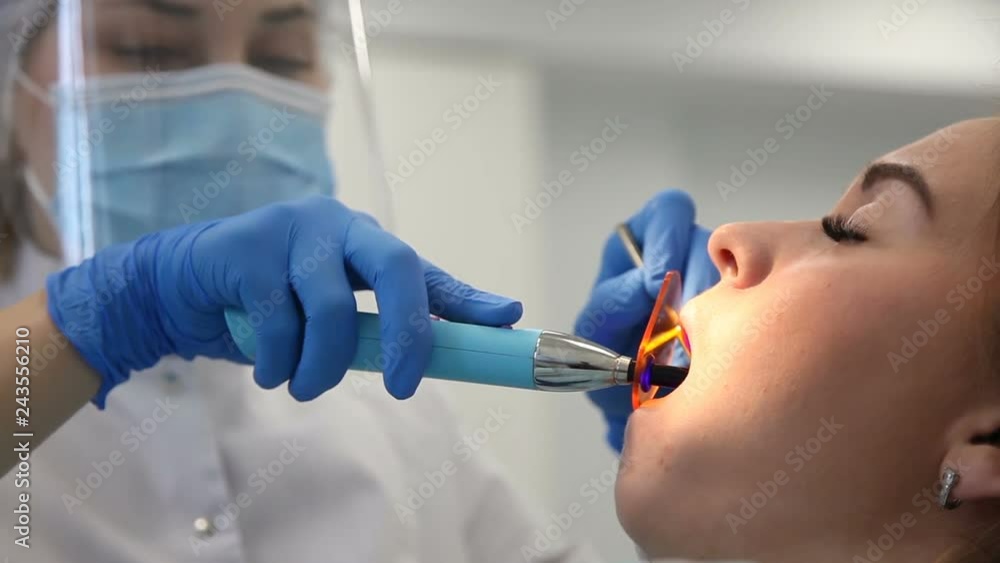 Female dentist work with light-curing seal, patient with caries on chair. Stomatologist and patient at clinical office. Toothcare concept Female dentist work with light-curing seal, patient with caries on chair. Stomatologist and patient at clinical office. Toothcare concept