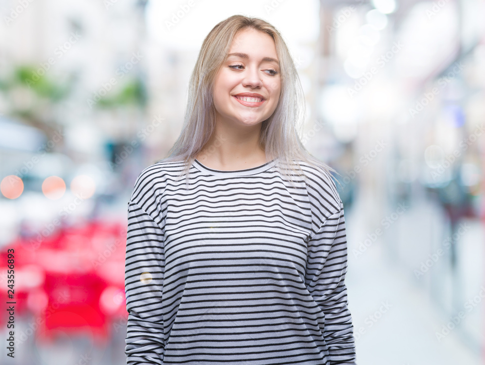 Young blonde woman over isolated background looking away to side with smile on face, natural expression. Laughing confident.
