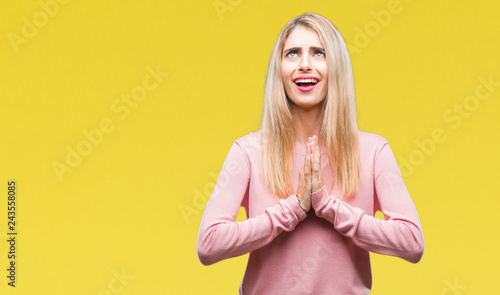 Young beautiful blonde woman wearing pink winter sweater over isolated background begging and praying with hands together with hope expression on face very emotional and worried