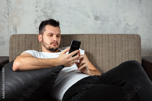 The guy in the white shirt is lying on the couch and sitting in the phone. The concept of laziness, apathy, frustration, procrastination, the person at home. copy space. photo