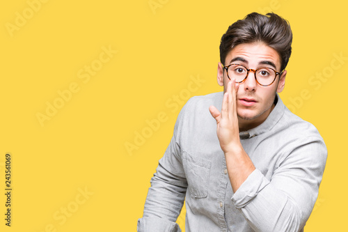 Young handsome man wearing glasses over isolated background hand on mouth telling secret rumor, whispering malicious talk conversation photo