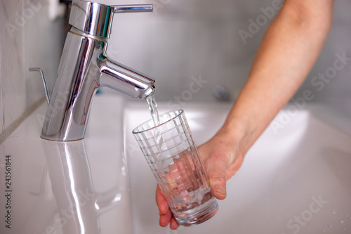 Hand with glass under running tap
