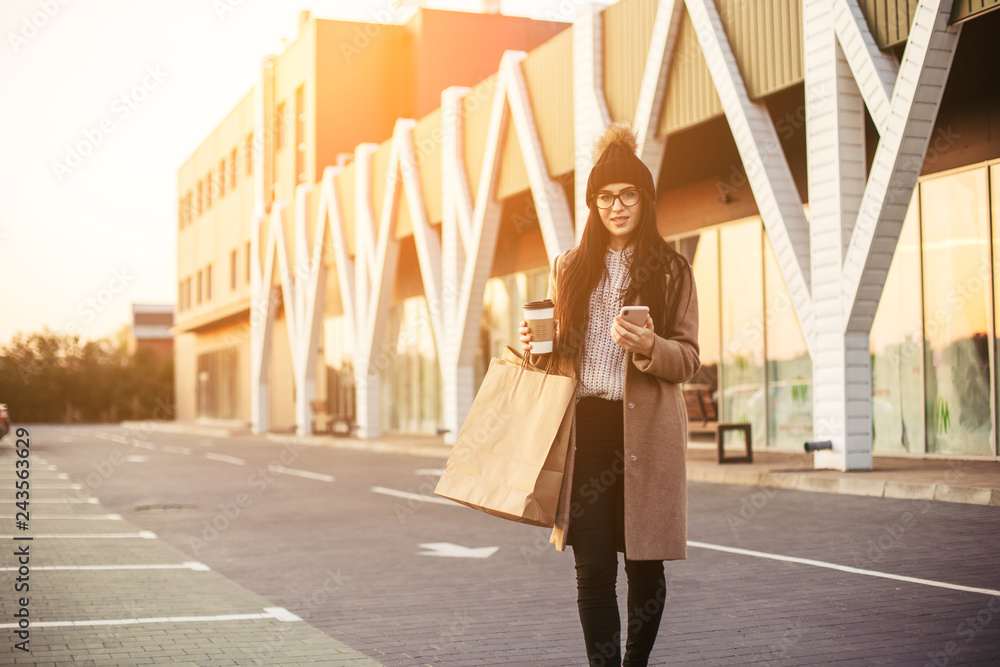 Young trendy woman blogger with shopping bag and smartphone near mall Young trendy woman blogger with shopping bag and smartphone near mall