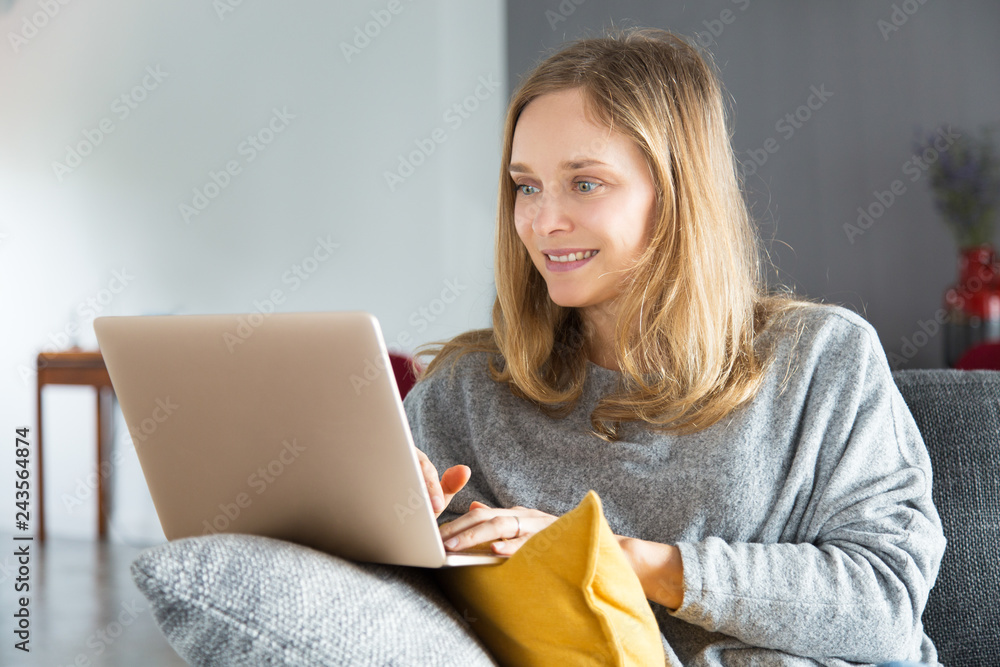Excited shopper purchasing online. Positive young woman sitting on couch, using laptop and smiling at monitor. Internet shopping concept Excited shopper purchasing online. Positive young woman sitting on couch, using laptop and smiling at monitor. Internet shopping concept