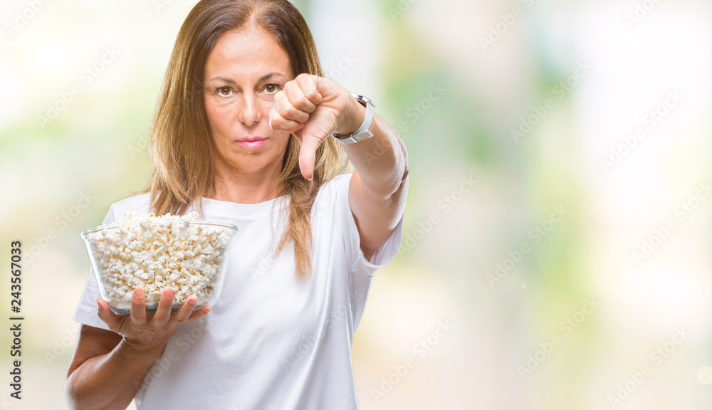 Middle age hispanic woman eating popcorn over isolated background with angry face, negative sign showing dislike with thumbs down, rejection concept Middle age hispanic woman eating popcorn over isolated background with angry face, negative sign showing dislike with thumbs down, rejection concept