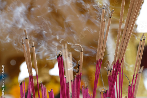 Burning incense and its smoke in front of  blurred golden Hindu Lord Brahma or Phra Phrom statue and yellow floral garland. Pray for spiritual healing and good Karma. Wishing for magic and answers. photo