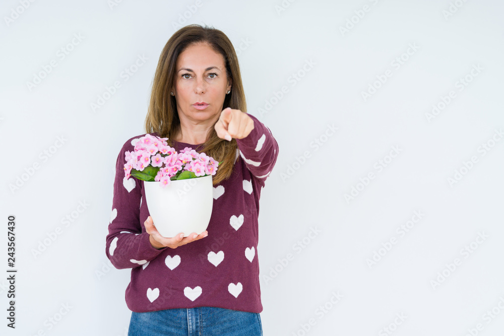 Middle age woman holding flowers pot plant over isolated background pointing with finger to the camera and to you, hand sign, positive and confident gesture from the front Middle age woman holding flowers pot plant over isolated background pointing with finger to the camera and to you, hand sign, positive and confident gesture from the front
