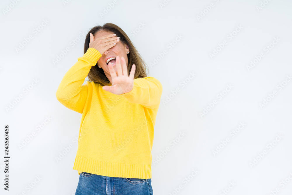 Beautiful middle age woman wearing yellow sweater over isolated background covering eyes with hands and doing stop gesture with sad and fear expression. Embarrassed and negative concept. Beautiful middle age woman wearing yellow sweater over isolated background covering eyes with hands and doing stop gesture with sad and fear expression. Embarrassed and negative concept.