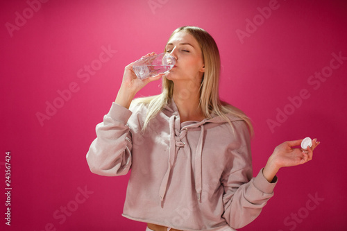 Young woman with a bottle of drinking water on a pink background