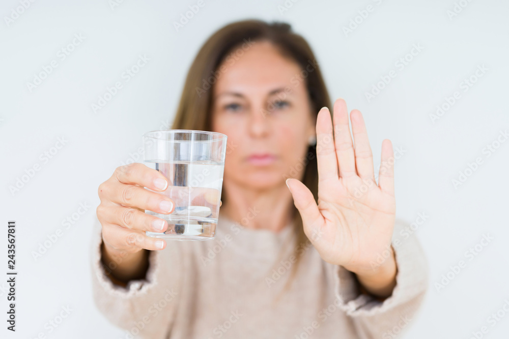 Middle age woman drinking glass of water isolated background with open hand doing stop sign with serious and confident expression, defense gesture Middle age woman drinking glass of water isolated background with open hand doing stop sign with serious and confident expression, defense gesture