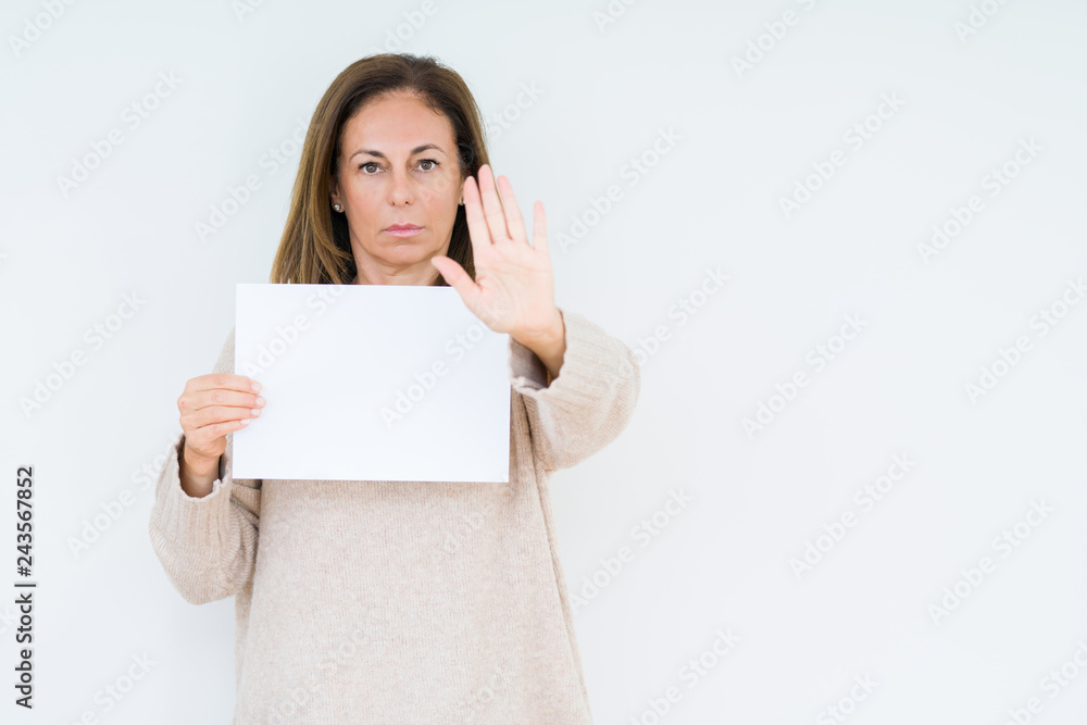 Middle age woman holding blank paper sheet over isolated background with open hand doing stop sign with serious and confident expression, defense gesture Middle age woman holding blank paper sheet over isolated background with open hand doing stop sign with serious and confident expression, defense gesture