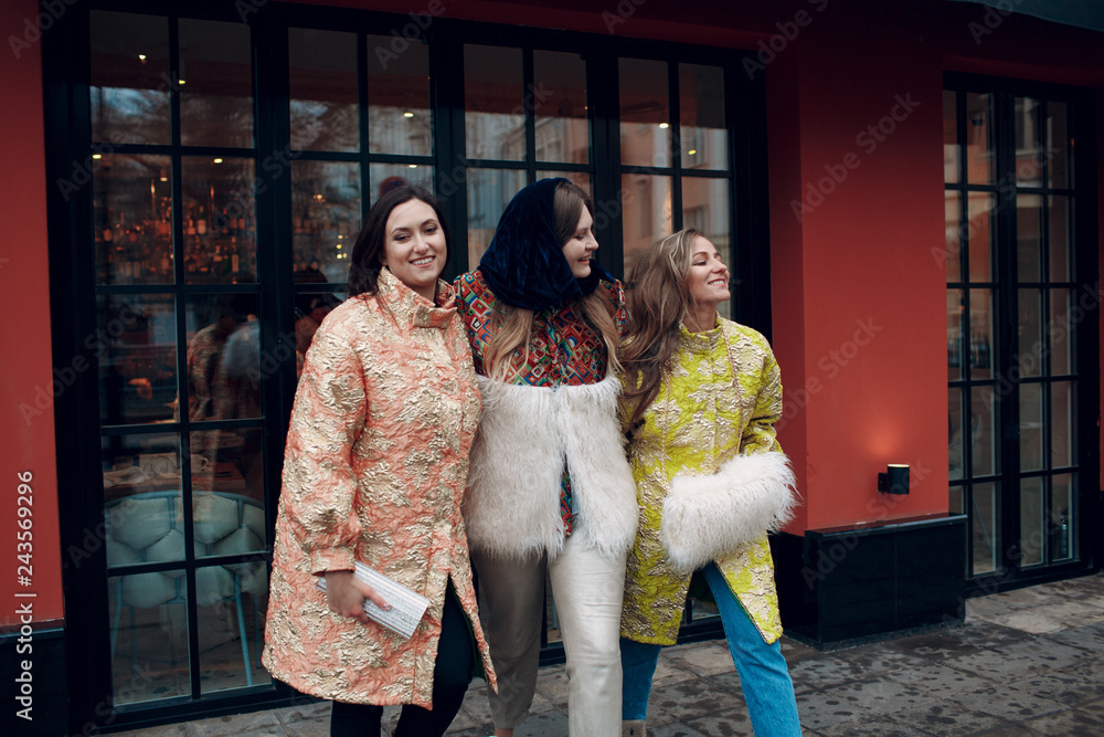 Three young stylish women are laughing and walking down the street.