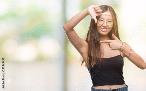 Young asian woman wearing glasses over isolated background smiling making frame with hands and fingers with happy face. Creativity and photography concept.