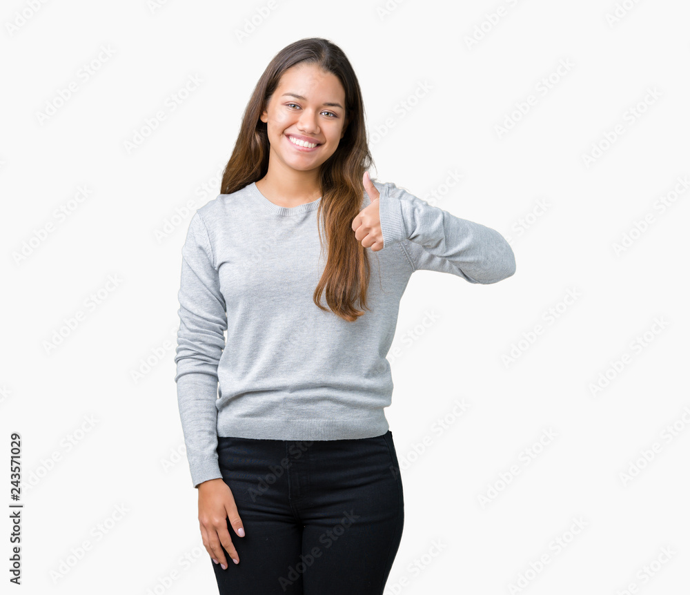 Young beautiful brunette woman wearing sweater over isolated background doing happy thumbs up gesture with hand. Approving expression looking at the camera with showing success. Young beautiful brunette woman wearing sweater over isolated background doing happy thumbs up gesture with hand. Approving expression looking at the camera with showing success.
