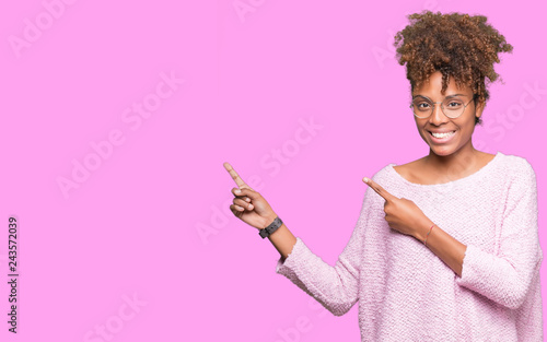 Beautiful young african american woman wearing glasses over isolated background smiling and looking at the camera pointing with two hands and fingers to the side.