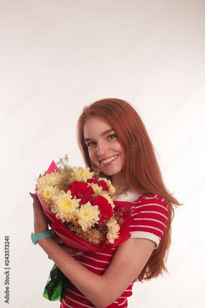 The portrait of smiling young redhead lady with flowers isolated over white wall background wearing colorful bright dress looking camera The portrait of smiling young redhead lady with flowers isolated over white wall background wearing colorful bright dress looking camera