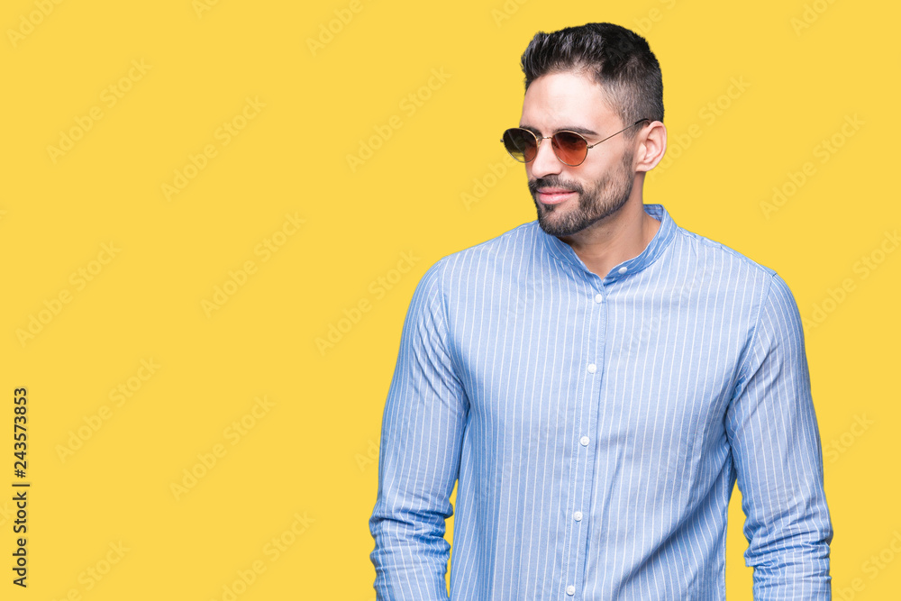 Young handsome man wearing sunglasses over isolated background looking away to side with smile on face, natural expression. Laughing confident. Young handsome man wearing sunglasses over isolated background looking away to side with smile on face, natural expression. Laughing confident.