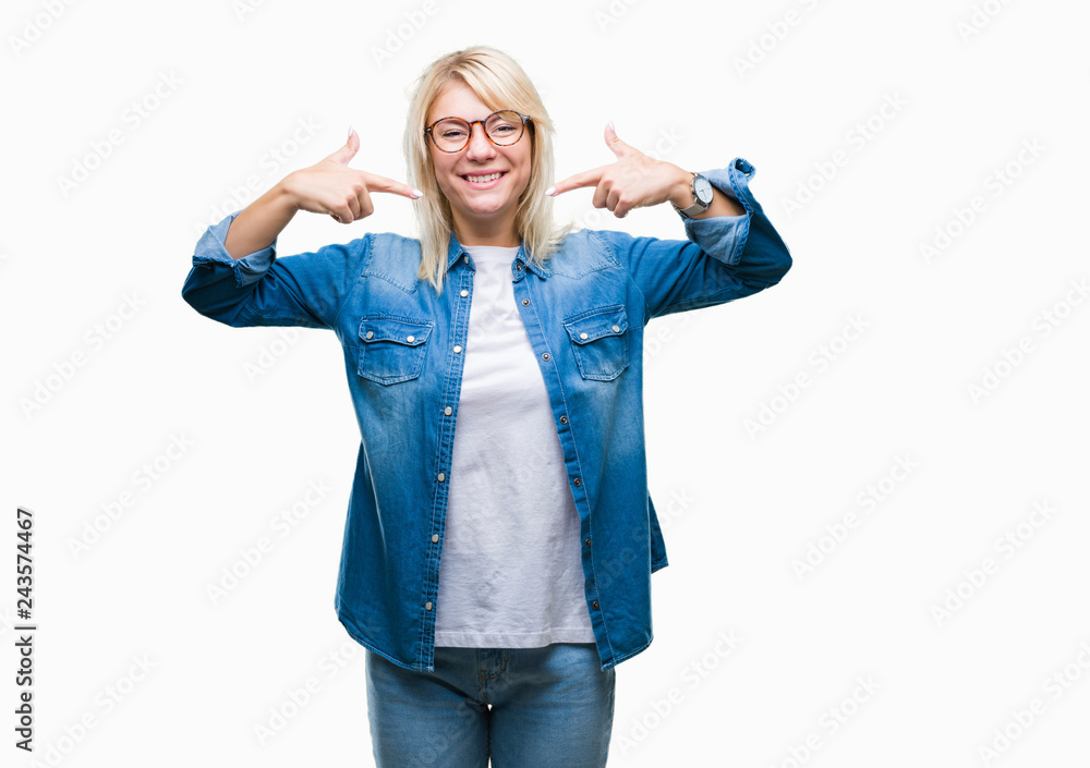 Obraz premium Young beautiful blonde woman wearing glasses over isolated background smiling confident showing and pointing with fingers teeth and mouth. Health concept.