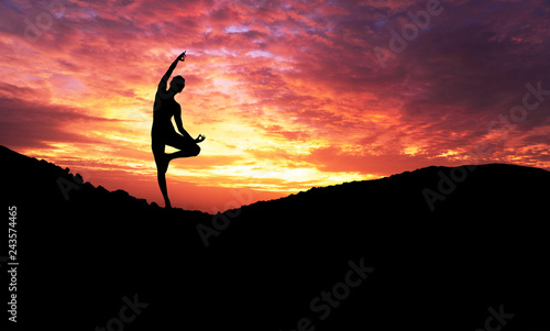 Silhouette of healthy young woman practicing yoga meditation during on background mountain with sky and sunset.