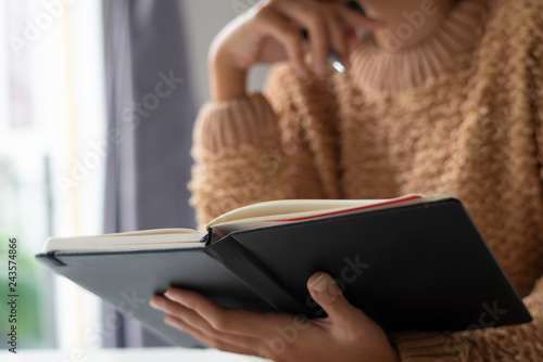 Close-up of unrecognizable woman reading note in personal organizer. Busy lady n sweater thinking about tasks and plans. Purposes concept