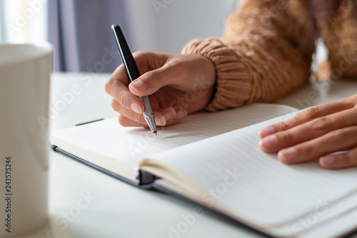 Close-up of woman sitting at table and planning schedule. Unrecognizable lady making notes in diary. Tasks concept