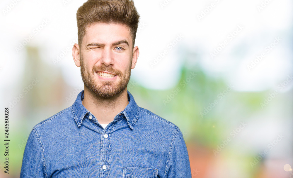 Young handsome blond man wearing casual denim shirt winking looking at the camera with sexy expression, cheerful and happy face. Young handsome blond man wearing casual denim shirt winking looking at the camera with sexy expression, cheerful and happy face.