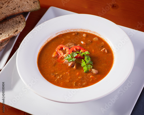 Delicious hungarian goulash soup with garnish served in a white plate on a wooden table