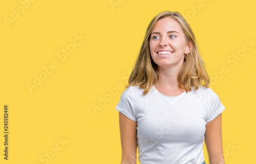 Beautiful young woman wearing casual white t-shirt over isolated background looking away to side with smile on face, natural expression. Laughing confident.