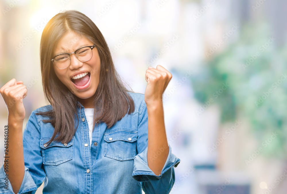 Young asian woman wearing glasses over isolated background very happy and excited doing winner gesture with arms raised, smiling and screaming for success. Celebration concept. Young asian woman wearing glasses over isolated background very happy and excited doing winner gesture with arms raised, smiling and screaming for success. Celebration concept.
