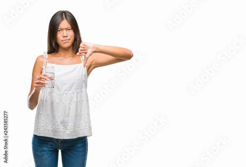 Young asian woman drinking glass of water over isolated background with angry face, negative sign showing dislike with thumbs down, rejection concept