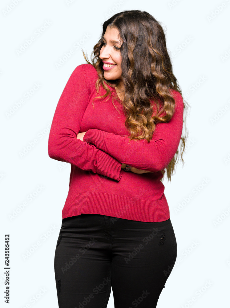 Young beautiful woman wearing red sweater smiling looking to the side with arms crossed convinced and confident Young beautiful woman wearing red sweater smiling looking to the side with arms crossed convinced and confident