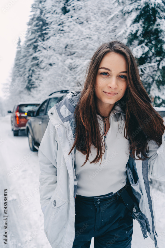 Beautiful young brunette woman in ski suit walking on the winter road near the snowy forest. Portrait shot Beautiful young brunette woman in ski suit walking on the winter road near the snowy forest. Portrait shot