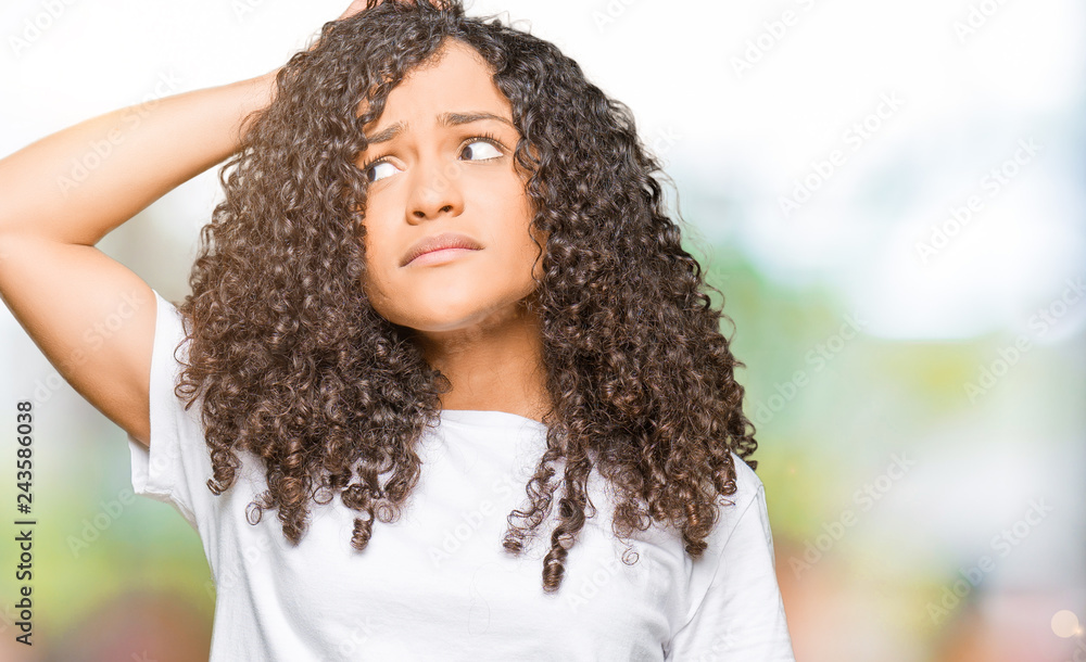 Young beautiful woman with curly hair wearing white t-shirt confuse and wonder about question. Uncertain with doubt, thinking with hand on head. Pensive concept. Young beautiful woman with curly hair wearing white t-shirt confuse and wonder about question. Uncertain with doubt, thinking with hand on head. Pensive concept.