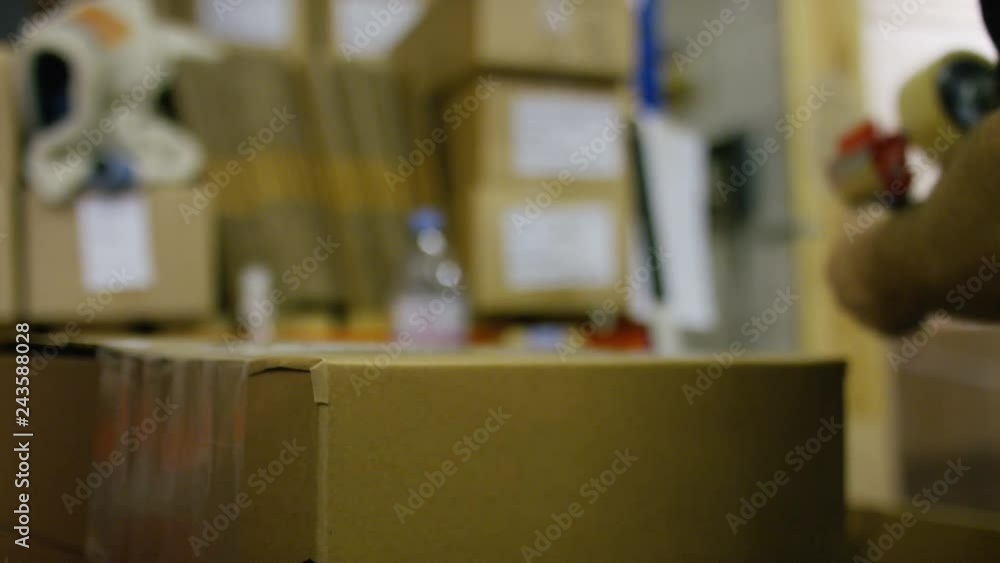 Hands of a warehouse worker taping up a box for delivery