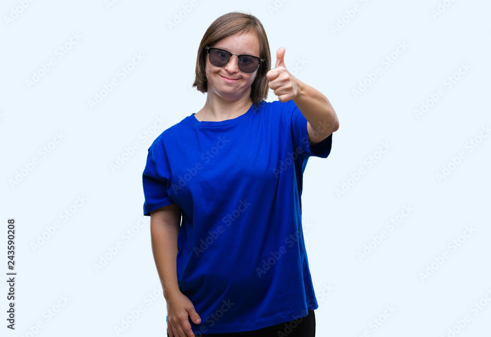 Young adult woman with down syndrome wearing sunglasses over isolated background doing happy thumbs up gesture with hand. Approving expression looking at the camera with showing success. Young adult woman with down syndrome wearing sunglasses over isolated background doing happy thumbs up gesture with hand. Approving expression looking at the camera with showing success.