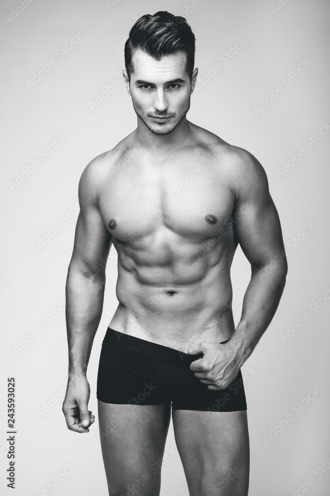 Fototapeta premium Portrait of handsome young man with stylish haircut in white underwear posing over gray background. Perfect hair & skin. Close up. Studio shot