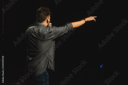 hombre joven blanco cantando en escenario con micrófono en mano con fondo negro