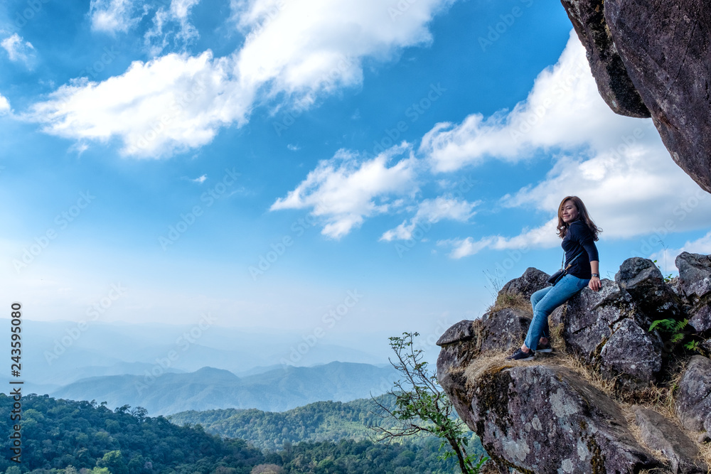 A beautiful asian woman sitting on a cliff with mountains view and blue sky background