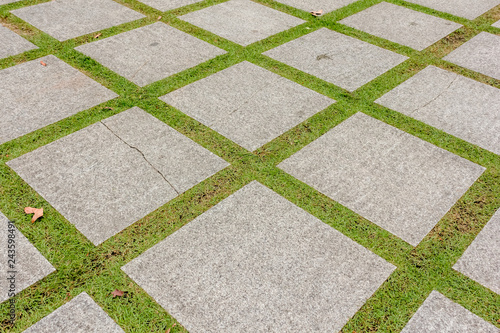 Pattern of square cement floor tiles with green grass field, perspective view. © DesignStory