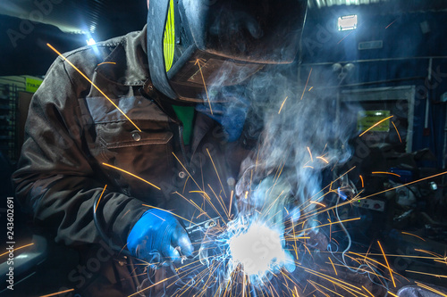 Obraz na plátne Man welder in welding mask, building uniform and blue protective gloves welds me