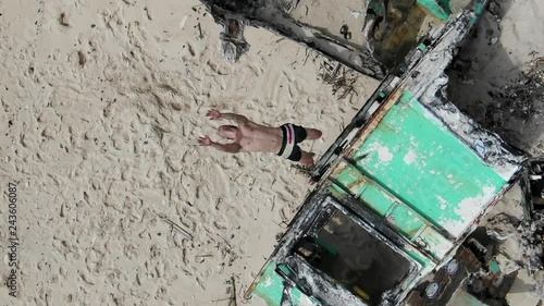 A Man Backflips from on top of a Graffiti Covered Structure on a Beach, Falls Down and Laughs in Slow Motion, Overhead Angle photo