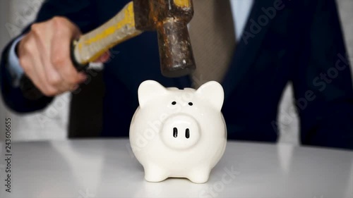 Business man Closeup breaking white piggy bank with a hammer and coins scattered everywhere in slow motion