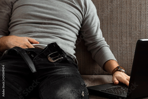 A man watches an adult video on a laptop while sitting on the couch. The concept of porn  masturbation  male needs  pervert  lust  desire  loneliness.