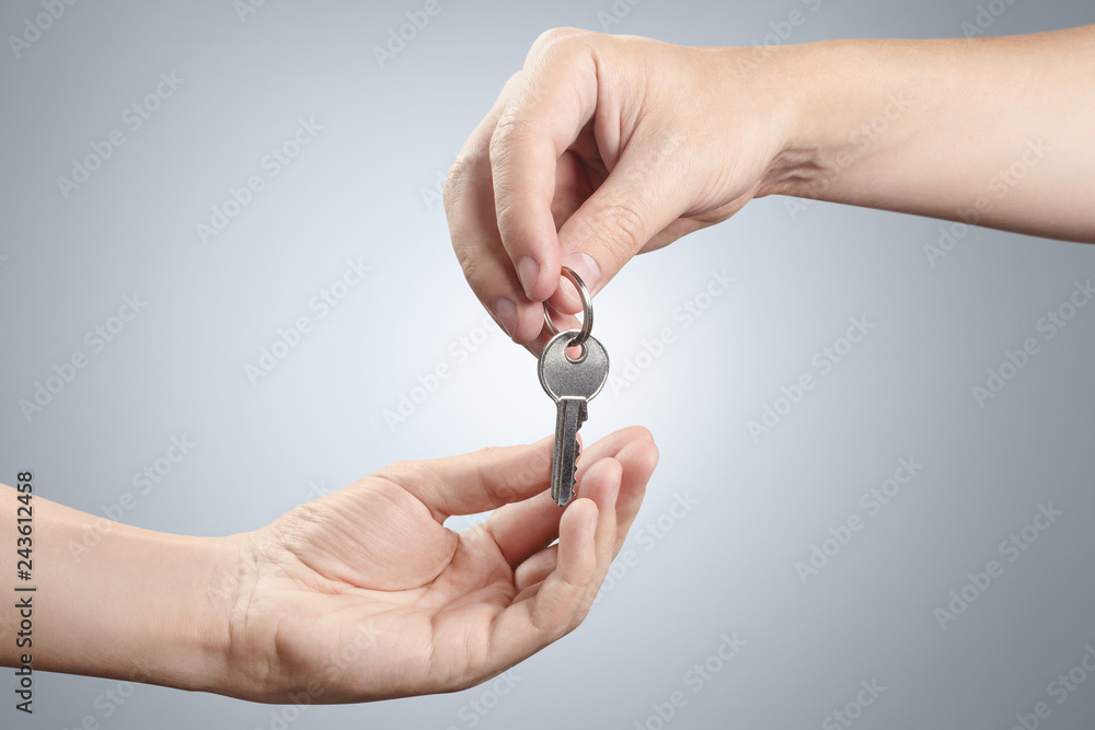 Hands of two people, giving and taking keys on gray background Hands of two people, giving and taking keys on gray background