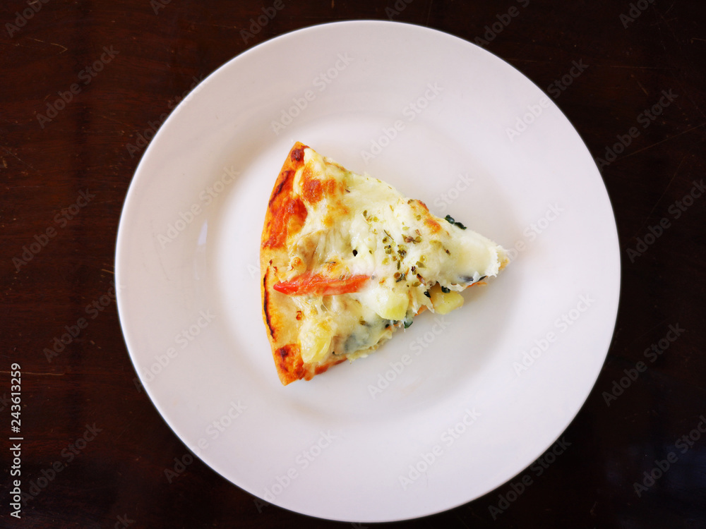 piece of pizza on white dish with dark brown table background. copyspace.